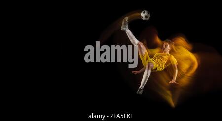 Un jeune homme du caucase, un joueur de football ou un joueur de football, donne un coup de pied au but dans une lumière mélangée sur fond sombre. Concept de mode de vie sain, professionnel Banque D'Images