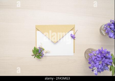 Carte, enveloppe et petites fleurs hepatica dans une bouteille en verre sur une table en bois. Violet Hepatica nobilis, Hepatica commun ou Anemone hepatica. Début de la spri Banque D'Images