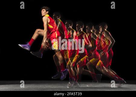 Jeune joueur de basket-ball caucasien en mouvement et en action dans une lumière mixte sur fond sombre. Concept de mode de vie sain, sport professionnel, passe-temps. Banque D'Images