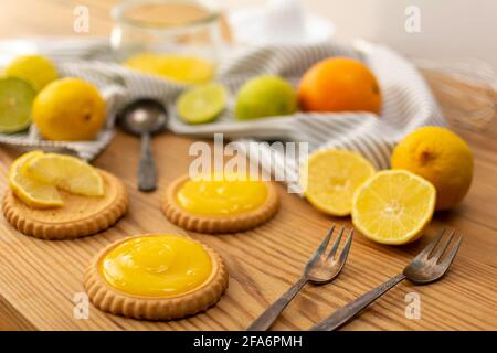 Quelques petits gâteaux frais cuits ou des gâteaux au citron, des ingrédients sur une table en bois comme des citrons, des oranges, des limes. Fourchettes et cuillères prêtes à être utilisées. Banque D'Images