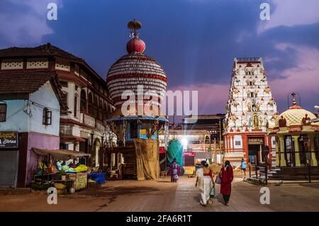 Udupi, Karnataka, Inde : deux femmes marchent avant l'aube vers le temple Krishna du XIIIe siècle et de grands chars processionnels à l'extérieur. Le temple était fou Banque D'Images