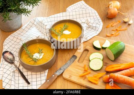 Un bon repas maison contenant une soupe de légumes frais avec des carottes et des courgettes et des oignons servis sur une vieille table en bois avec beaucoup de garniture. Banque D'Images