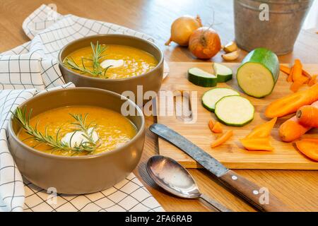 Un bon repas maison contenant une soupe de légumes frais avec des carottes et des courgettes et des oignons servis sur une vieille table en bois avec beaucoup de garniture. Banque D'Images