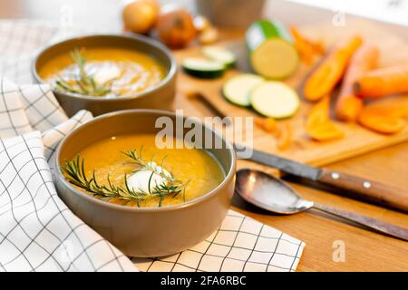 Un bon repas maison contenant une soupe de légumes frais avec des carottes et des courgettes et des oignons servis sur une vieille table en bois avec beaucoup de garniture. Banque D'Images