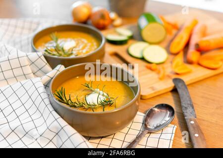 Un bon repas maison contenant une soupe de légumes frais avec des carottes et des courgettes et des oignons servis sur une vieille table en bois avec beaucoup de garniture. Banque D'Images