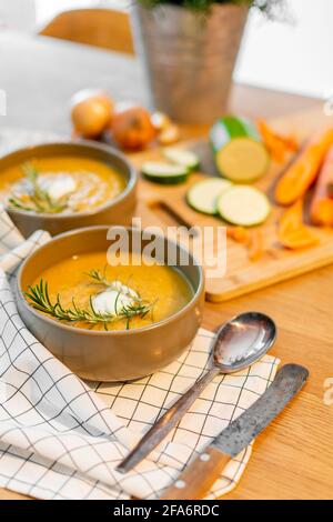 Un bon repas maison contenant une soupe de légumes frais avec des carottes et des courgettes et des oignons servis sur une vieille table en bois avec beaucoup de garniture. Banque D'Images