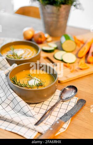 Un bon repas maison contenant une soupe de légumes frais avec des carottes et des courgettes et des oignons servis sur une vieille table en bois avec beaucoup de garniture. Banque D'Images