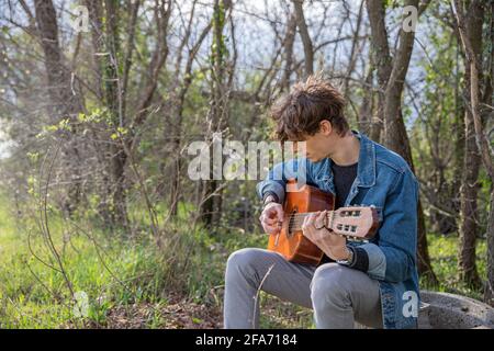 Un sympathique gars joue de la guitare dans une forêt Banque D'Images