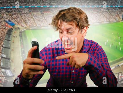 composite conceptuel avec homme heureux et excité avec téléphone mobile et de l'arrière-plan de football dans le pari de sport en ligne et le jeu d'internet concept gagnant et Banque D'Images