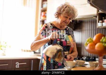 Femme âgée avec une bouilloire qui verse de l'eau chaude dans une tasse cuisine Banque D'Images