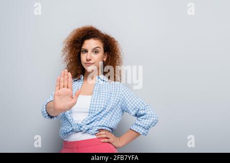 une femme mécontentue de montrer un geste de refus en se tenant debout à la main hanche sur fond gris Banque D'Images