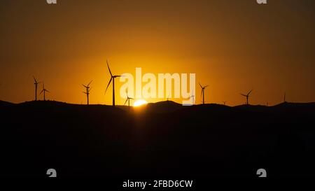 Le soleil se couche sur les montagnes avec les silhouettes des éoliennes comme protagonistes. Banque D'Images