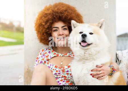 REDHEAD femme souriant assis avec un chien devant pilier Banque D'Images