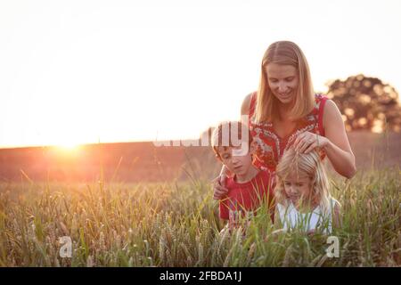 Garçon et fille regardant les plantes devant la mère sur le terrain agricole Banque D'Images