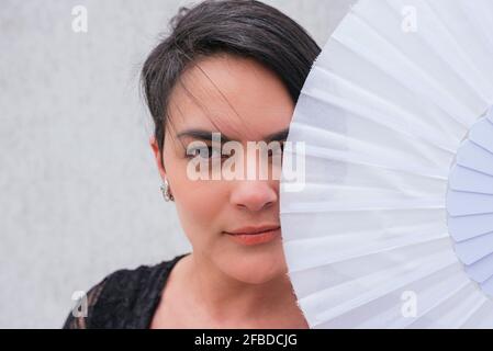 Femme caucasienne couvrant le visage avec un ventilateur à main devant mur Banque D'Images