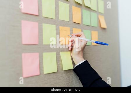 Une femme entrepreneur écrit sur des notes adhésives fixées sur un mur beige Banque D'Images