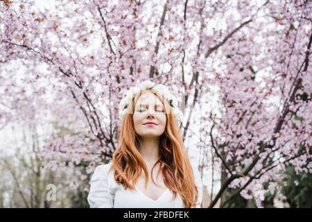 Jeune femme avec les yeux fermés portant le tiara de fleur blanc debout devant l'amandier Banque D'Images