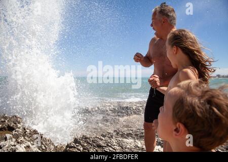 Père avec des enfants regardant les éclaboussures d'eau tout en étant debout rock Banque D'Images