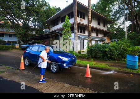 Un homme nettoie la route avec un tuyau d'eau à l'extérieur de sa maison dans la ville de Gamboa, province de Colon, République du Panama, Amérique centrale. Banque D'Images