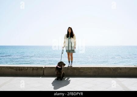 Une femme heureuse avec un chien debout sur le mur de retenue à l'avant de mer Banque D'Images