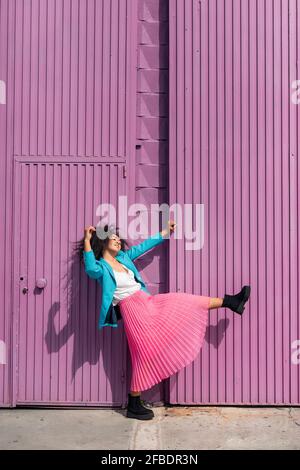 Jeune femme ludique dansant au mur de la cabine mauve par beau temps Banque D'Images