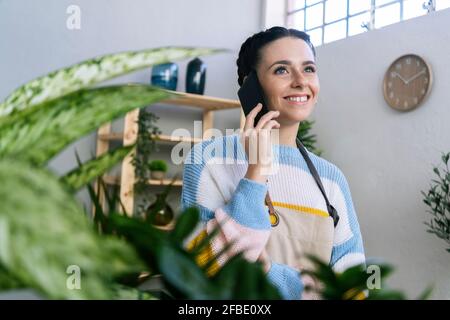 Une jardinière souriante parle au téléphone intelligent dans un atelier Banque D'Images