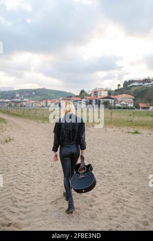 Jeune femme guitariste marchant sur du sable transportant de la guitare Banque D'Images