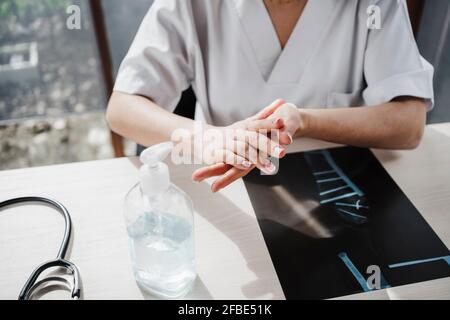 Une femme médecin se frottant les mains ensemble tout en appliquant de l'assainisseur au bureau Banque D'Images