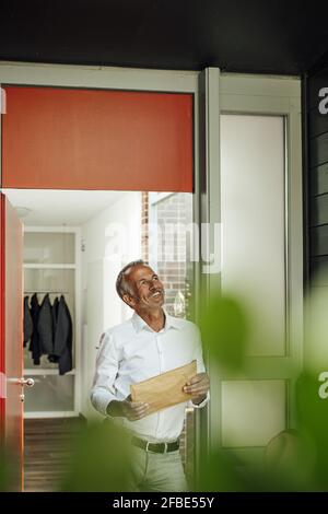 Homme souriant et attentionné tenant le paquet tout en s'inclinant à la porte Banque D'Images