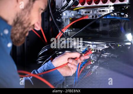 Un spécialiste INFORMATIQUE de sexe masculin installe le cordon de raccordement dans le rack de serveur dans le centre de données Banque D'Images