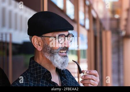 Homme mûr heureux tenant le tuyau de cigarette tout en regardant loin Banque D'Images