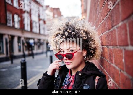 Femme aux cheveux bouclés portant des lunettes de soleil au mur à Chinatown pendant vacances Banque D'Images
