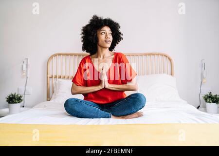 Femme regardant loin en étant assise avec les mains clastées sur le lit à la maison Banque D'Images