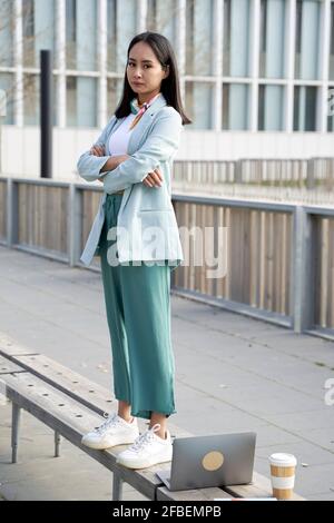 Femme d'affaires avec les bras croisés debout sur le banc au niveau de la piste de marche Banque D'Images