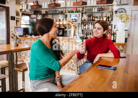 Des amies gaies toastent des bouteilles de bière au bar Banque D'Images