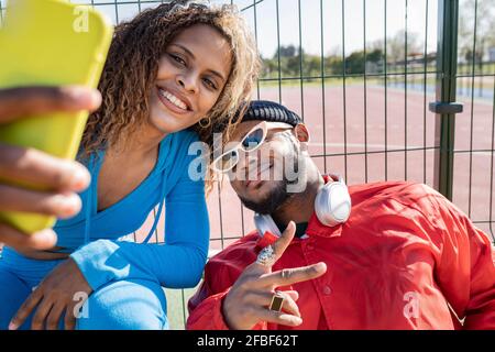 Homme montrant le signe de la paix tout en prenant le selfie avec une amie femelle sur le terrain de sport Banque D'Images