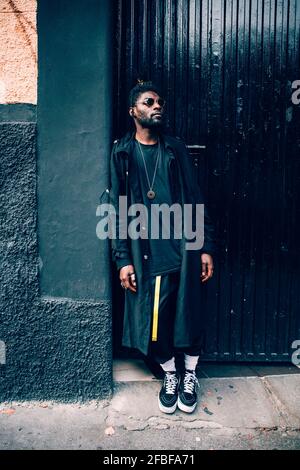 Jeune homme à la mode regardant loin en s'inclinant sur le mur Banque D'Images
