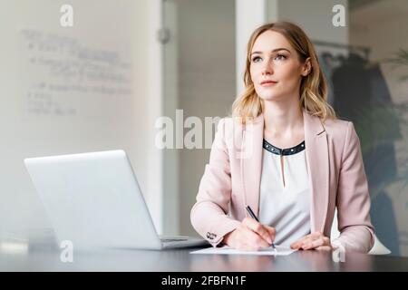 Femme d'affaires qui envisage de rédiger un document sur un ordinateur portable au bureau Banque D'Images