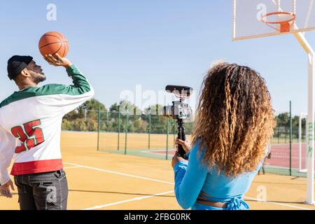 Une femme filmant un ami jouant au basket-ball sur un terrain de sport Banque D'Images