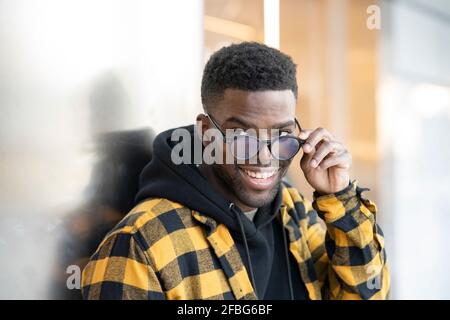 Jeune homme souriant tenant des lunettes tout en regardant loin Banque D'Images