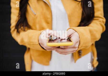 Femme adulte de taille moyenne dans une veste jaune messagerie texte par SMART téléphone Banque D'Images