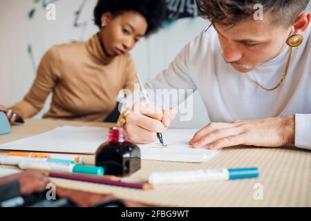 Un homme de taille basse écrit avec un stylo plume sur le papier tout en étant assis par femme en studio Banque D'Images