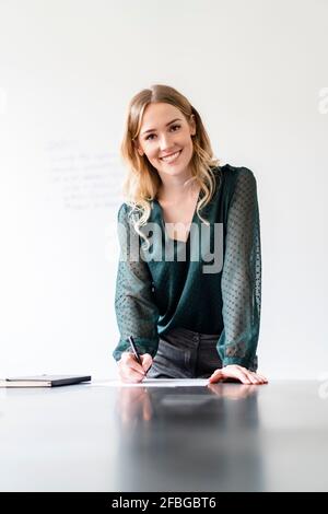 Femme entrepreneure souriante écrivant sur un document au bureau Banque D'Images