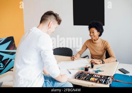 Femme souriante regardant l'homme tout en pratiquant la calligraphie à la table en studio Banque D'Images