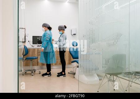 Assistant aidant le médecin à s'habiller avec des vêtements de protection en clinique Pendant COVID-19 Banque D'Images