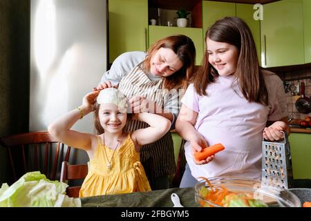 Une mère ludique et des filles souriantes préparent la nourriture dans la cuisine à accueil Banque D'Images