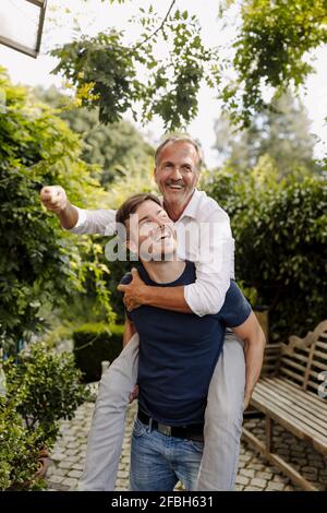 Un fils joyeux qui donne une promenade en pigeyback à son père dans l'arrière-cour Banque D'Images