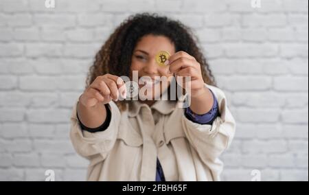Femme souriante montrant des bitcoins argentés et dorés devant le mur Banque D'Images