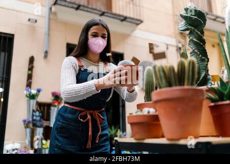 Jeune fleuriste femelle avec masque protecteur tenant une plante en pot en magasin Banque D'Images