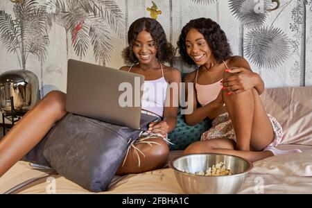 Portrait de deux amis heureux assis ensemble sur le lit à regarder un film à la maison Banque D'Images